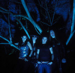 Sirenia-yhtye sinisävyisessä kuvassa, taustalla puiden karahkoja. Vasemmassa laidassa bändin naispuolinen laulaja.