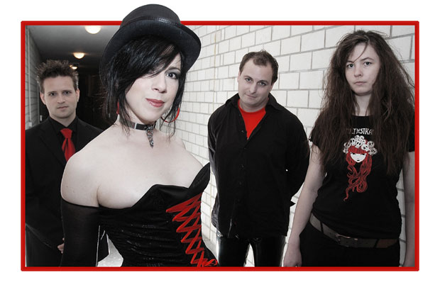 Valokuva The Slimpin joukosta. Kuvassa kaksi naista etualalla ja heidän takanaan kaksi miestä. Kaikki ovat mustapunaisiin vaatteisiin pukeutuneita. Naisella etualalla hihaton musta korsetti yllään ja kalpea iho, musta silinterihattu päässään.