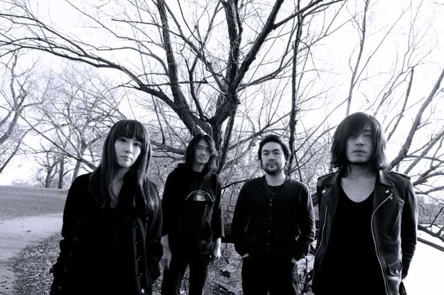 Harmaasävyinen valokuva Mono-nimisestä japanilaisbändistä, johon kuuluu neljä muusikkoa. Kolme muusikoista miehiä, mutta vasemman laidan henkilö nainen. Kaikilla mustaa vaatetta yllään. He seisovat elottomien puiden edessä kylmän taivaan alla.