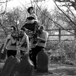 Harmaasävyinen valokuva Zombina and the Skeletonesin kokoonpanoon kuuluvista ihmisistä, jotka puolialastomina haahuilevat hautakivien seassa kanniskellen naista kantotuolissa.