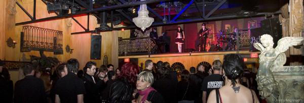 Valokuva Tranzylvania-goottiklubilla esiintyvästä Bella Lunesta, sekä suuresta ihmislaumasta tapahtumapaikan yleisönä. Hallissa on patsaita ja koriste-esineitä pitkin seiniä.