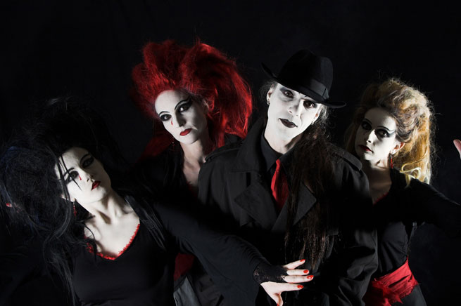 Mustaa taustaa vasten mies ja kolme naista. Kullakin ihmisellä valkoisiksi maalatut kasvot ja pääosin mustat vaatteet, mutta osalla vaatteissa punaisia tehostevärejä. Keskimmäinen hahmo on lakkipäinen mies.