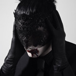 Shiv-r:n Pete harmaata taustaa vasten mustiin pukeutuneena. Miehellä mustat hiukset, kalpeat kasvot ja kasvojen päällä jonkinlainen kangaspala. Miehellä myös mustat nahkahansikkaat, jotka laitettu korville.