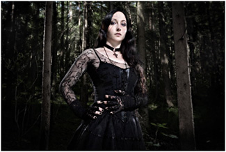 Mustaan goottimekkoon pukeutunut mustahiuksinen goottinainen seisoo uhkaavan tumman kuusimetsän siimeksessä katsellen loivasti alaspäin. Naisella koristeelliset käsivarsihihat.