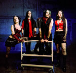 Jesus On Extasy -bändin jäsenet, eli kaksi naista ja kaksi miestä, seisovat vuoteen äärellä. Taustalla hämyistä sinertävää taustaväriä.