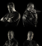 Harmaasävyinen ryhmäkuva neljästä mustiin pukeutuneesta miehestä, jotka sijoitettu kuvan neljään kulmaan. Kuvan tausta on musta.