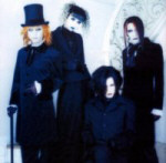 Malice Mizer -bändin jäsenet mustiin asuihin pukeutuneina. Yhdellä miehistö silinterihattu ja kävelykeppi.