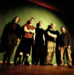 Front Line Assembly -bändin jäsenet seisovat vihreää seinää vasten. Lattia on tummaa puuta. Kuvakulma ruohonjuuritasolla.