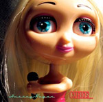 Valokuva suuripäisestä muovinukesta, joka pitelee kourissaan mikrofonia. Kuvan alaosassa lukee Hussey-Regan ja "Curios".