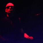 Soman-bändin jäsen seisoo mustat aurinkolasit silmillään hyvin tummasävyisessä kuvassa, jossa näkyy vain miehen kasvot ja osa käsivarresta.