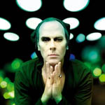 Valokuva miehestä, joka pitää käsiään leukansa alla yhteen liitettyinä. taustalla rivissä valopalloja.