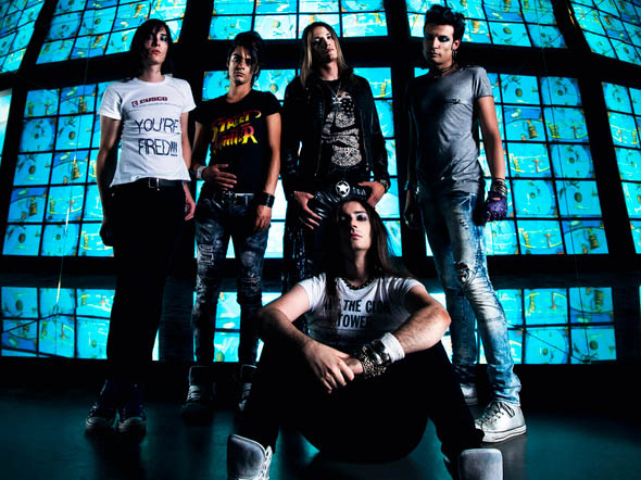 Sinisiä televisioruutuja, joita vasten Dope Stars Inc. -bändin viisi miestä seisovat etummaista lukuun ottamatta. Hän istuu muiden edessä.