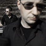 Edge Of Dawn -yhtyeen jäsenet, joista etualalla mustiin pukeutunut mies, jolla tummat aurinkolasit silmillään. Hänen takanaan, kauempana, istuu toinen mustiin vaatteisiin pukeutunut mies. Molemmilla lyhyet hiukset.