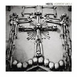 Valokuva rististä, joka rakennettu luista. Luuristissä ihmisen luita, pääkalloja. Kuvan oikeassa yläkulmassa mustalla värillä valkoista taustaa vasten Hecq-nimi.