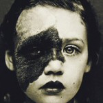 Harmaasävyinen valokuva lapsen kasvoista, joista toinen puoli on pikimusta ja likainen. Huuletkin on mustattu.