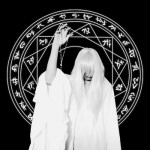 Mustavalkoinen valokuva henkilöstä, joka valkoiseen kaapuun pukeutuneena ojentelee kättään. Taustalla ympyrä, jossa erilaisia symboleita.