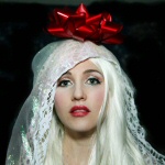 Valokuva naisesta, jolla valkoinen huntu pään yllä ja siihen kiinnitetty punainen lahjarusetti.