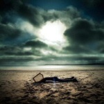 Valokuva myrskytaivaasta meren rannalla. Rannalla hiekan seassa lojuu jokin mytty.