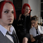 Kolmehenkisen Suicidal Romance -bändin jäsenet ryhmäpotretissa. Kuvassa vasemmassa laidassa etualalla mies, jolla vaalea kauluspaita, solmio, puolipitkät kirkkaanpunaiset hiukset ja hirviömäiset silmät. Taustalla kaksi naista.