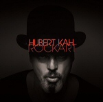 Mustaa taustaa vasten valokuva miehen kasvoista, jotka ovat varjojen ympäröimät ja osin peittämätkin. Kasvojen yllä punaisella värillä Hubert Kahin nimi.