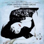 Sinimusta valokuvasta mustiin pukeutuneesta naisesta loikoilemassa. Kuvan yläosassa lukee mustalla: Lydia Lunch & Cypress Grove, sekä "Under the Covers" ilman lainausmerkkejä.