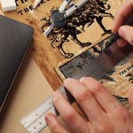 Valokuva viivottimen kanssa jotakin yksityiskohtaa piirtävästä henkilöstä.