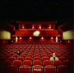 Voimakkaasti vinjetoitu valokuva teatterin katsomosta, jossa huimasti punaisia istuimia ja vain kaksi ihmistä istumassa.