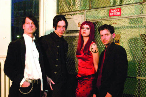 Neljä I:scintilla-bändin jäsentä poseeraa jonkinlaisessa sähköhuoneessa, jonka verkkoaitaa vasten he seisovat. Kuvassa kolme miestä ja yksi nainen, jolla pitkät punaiset hiukset ja punainen toppi sekä hame. Miehillä mustat hiukset.