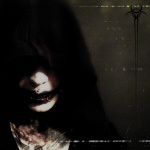 Mustaa taustaa vasten valokuva hämärähemmosta, jolla mustatut huulet ja kasvot pääosin mustan hupun peittämät.