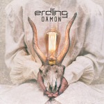 Valokuva tai piirros eläimen pääkallosta, jota valkoiseen pukuun puettu ihminen pitää käsin sylissään. Kallolla on pitkät pujot sarvet, ja kynttilä niiden v älissä.