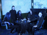 Sinisävyinen valokuva Eisheilig-yhtyeen jäsenistä, joita kuvassa viisi kappaletta. He istuvat pöydän ääressä. Kaikki ovat miehiä, heillä pitkät hiukset. Pukeutuneet pääsääntöisesti mustiin vaatteisiin.
