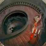 Faith Assemblyn maalausmainen kansikuva albumista 'Descent Into Madness', jossa näkyy suuren ympyränmuotoisen porraskäytävän laidalla nouseva kaapuun pukeutunut nainen, jolla kirkkaanpunaiset vaatteet ja hupullinen viitta yllään.