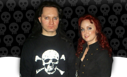 Amberian Dawnin kaksi päähenkilöä, mies ja nainen, seisovat koristeellista taustaa vasten. Vasemmalla mies, jolla pitkät mustat hiukset ja yllään musta paita, jossa valkoinen pääkallo. Oikealla puolella nainen, jolla tummanpunaiset laineilevat hi