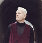 Attritionin Bowes seisoo mustaa taustaa vasten. Mies on keski-ikäinen. Hänellä vaaleat lyhyeksi leikatut hiukset. Bowesilla yllään musta poolopaita, jonka päällä tummanpunainen liivi.