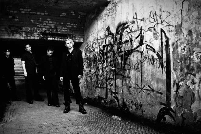 Mustavalkoinen promokuva vuodelta 2008, jossa kolmehenkisen Agonised By Loven miehistö seisoo spreijatun seinän vierustalla. Seinä on täynnä töhryjä. Miesten takana näkyy rappuset.