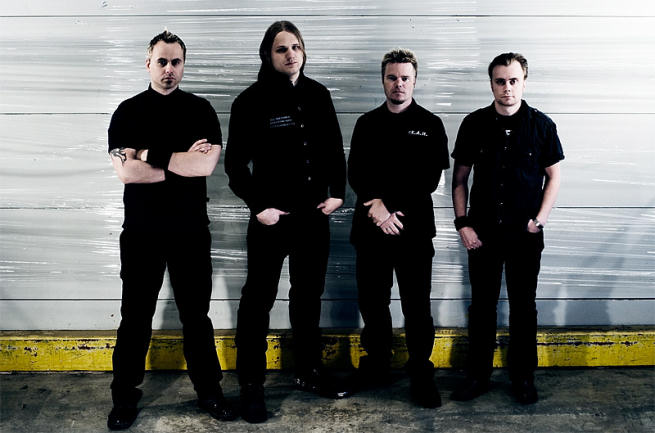 Kuva: Erik Jørgensen Promovalokuva Artifact-nimisen goottibändin miehistöstä, johon kuuluu neljä mustiin vaatteisiin sonnustautunutta heppua. Jokaisella samanlaiset vaatteety yllään. He seisovat jonkinlaista autotallin seinää vasten. Taustalla vaaleata, maarajassa kel