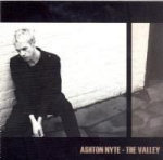 Valokuva Ashton Nytestä, jolla valkoiset hiukset ja musta emomainen olemus. Miehellä mustat vaatteet yllään. Hän istuu valkoista seinää vasten. Hänellä luisevat kädet. Kuvan ylä- ja alaosassa paksut mustat raidat. Kuvan oikeassa alakulmassa luk