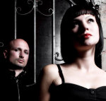 Valokuva kaksipäisestä Mina Harkerista. Vasemmassa laidassa taaempana näkyy kaljupäinen mies, jolla mustat vaatteet. Kuvan oikeassa laidassa seisoo mustiin pukeutunut nainen, jolla mustanvärinen polkkatukka ja punaisiksi värjätyt huulet, katse ylö